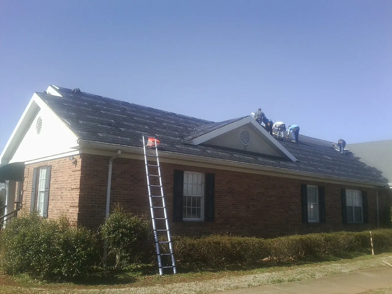Crew tearing shingles off a brick ranch roof with a ladder set — Metal Roof Repair work by our crew in Clarksburg