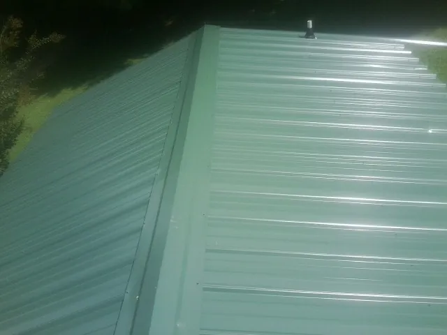 New green metal panels meeting at the ridge of a roof — Flat Roof Repair work by our crew in Clarksburg